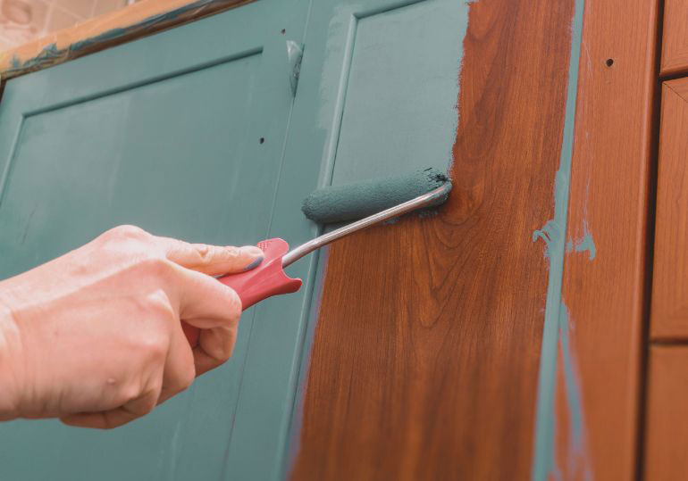 Photo of person painting over wood cabinets.